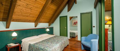 A bedroom with a wooden ceiling, a bed with a patterned bedspread, a chair, and a nightstand with a lamp.