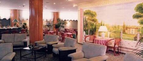 Eine Hotelhalle mit mehreren Sitzbereichen, einer Bar und einem Wandgemälde einer Landschaft.