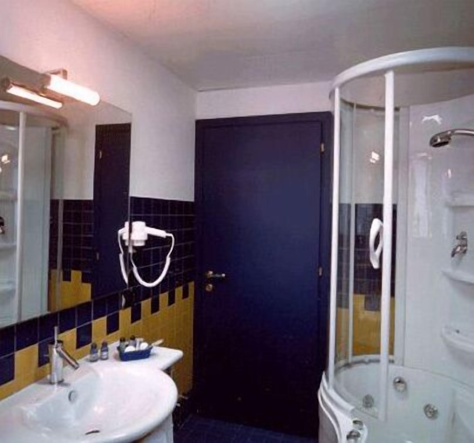 Un baño con lavamanos blanco, un espejo, una puerta azul oscuro y una ducha con cerramiento de vidrio.