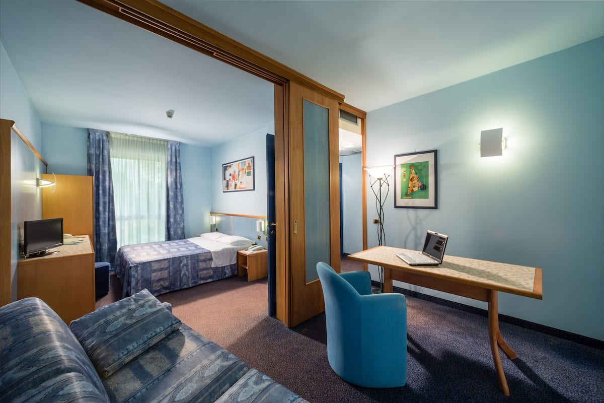 Ein Hotelzimmer mit einem Bett, einem Schreibtisch, einem Sessel, einer Couch und einem Kleiderschrank.