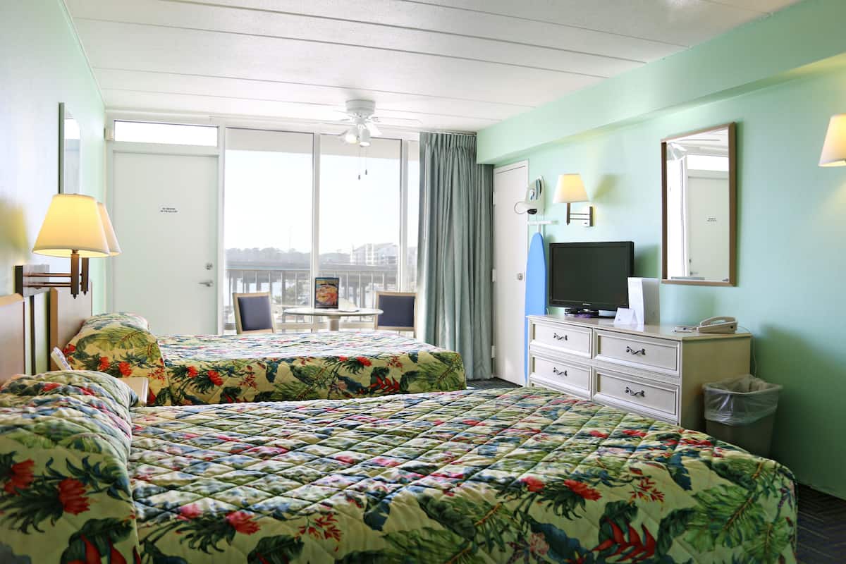 A hotel room with two beds, a television, a dresser, and a window with a view of buildings.