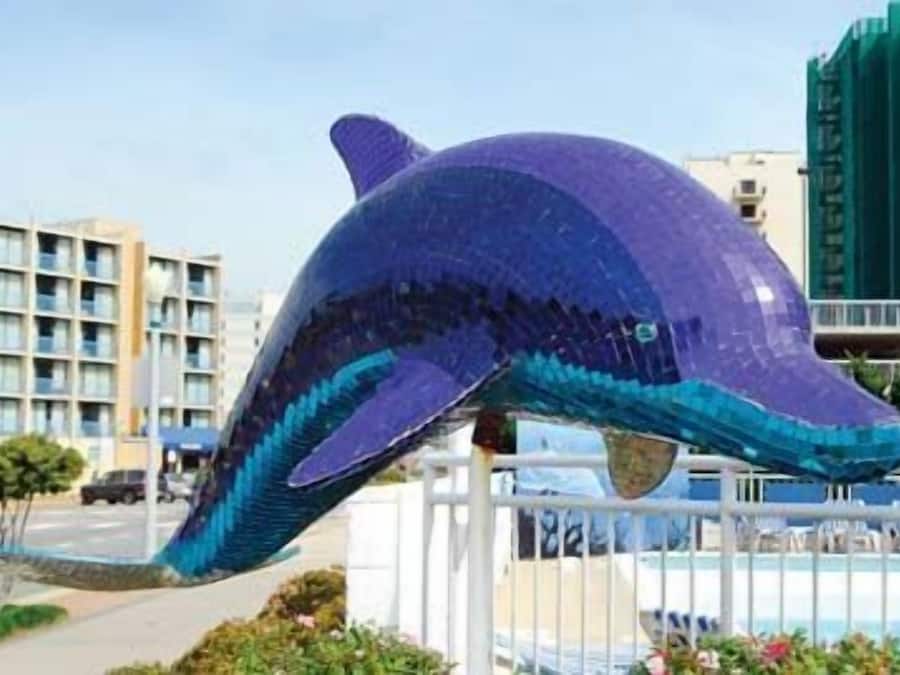 Een sculptuur van een dolfijn in een openbare ruimte, met gebouwen op de achtergrond.