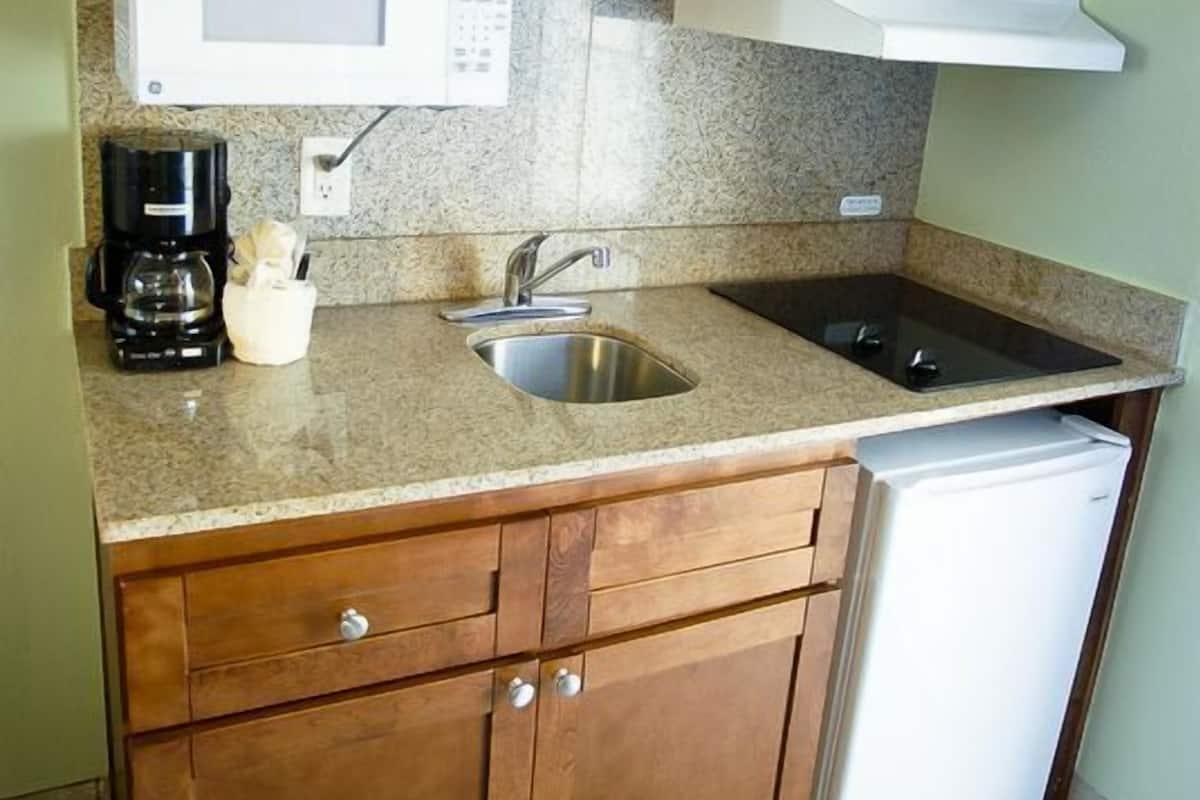 A compact kitchen with wooden cabinets, a built-in microwave, a sink, and a refrigerator.