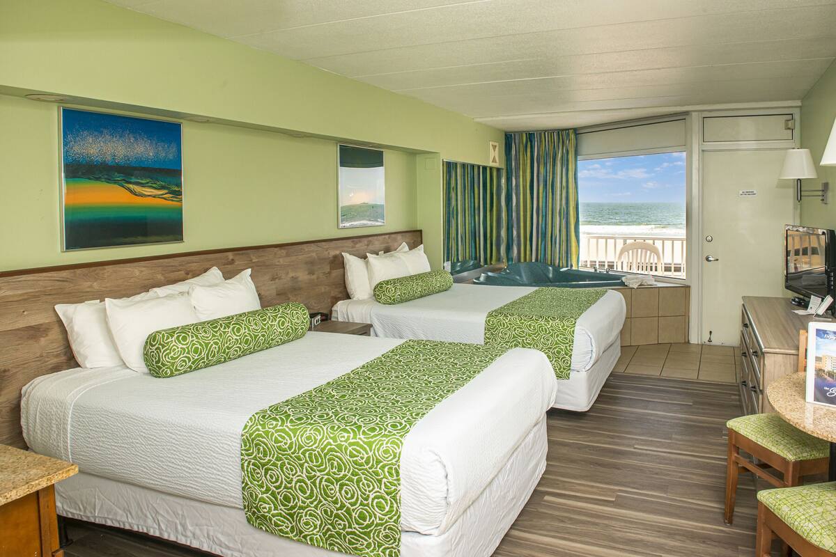 A hotel room with two beds, a desk, a chair, and a view of the ocean.