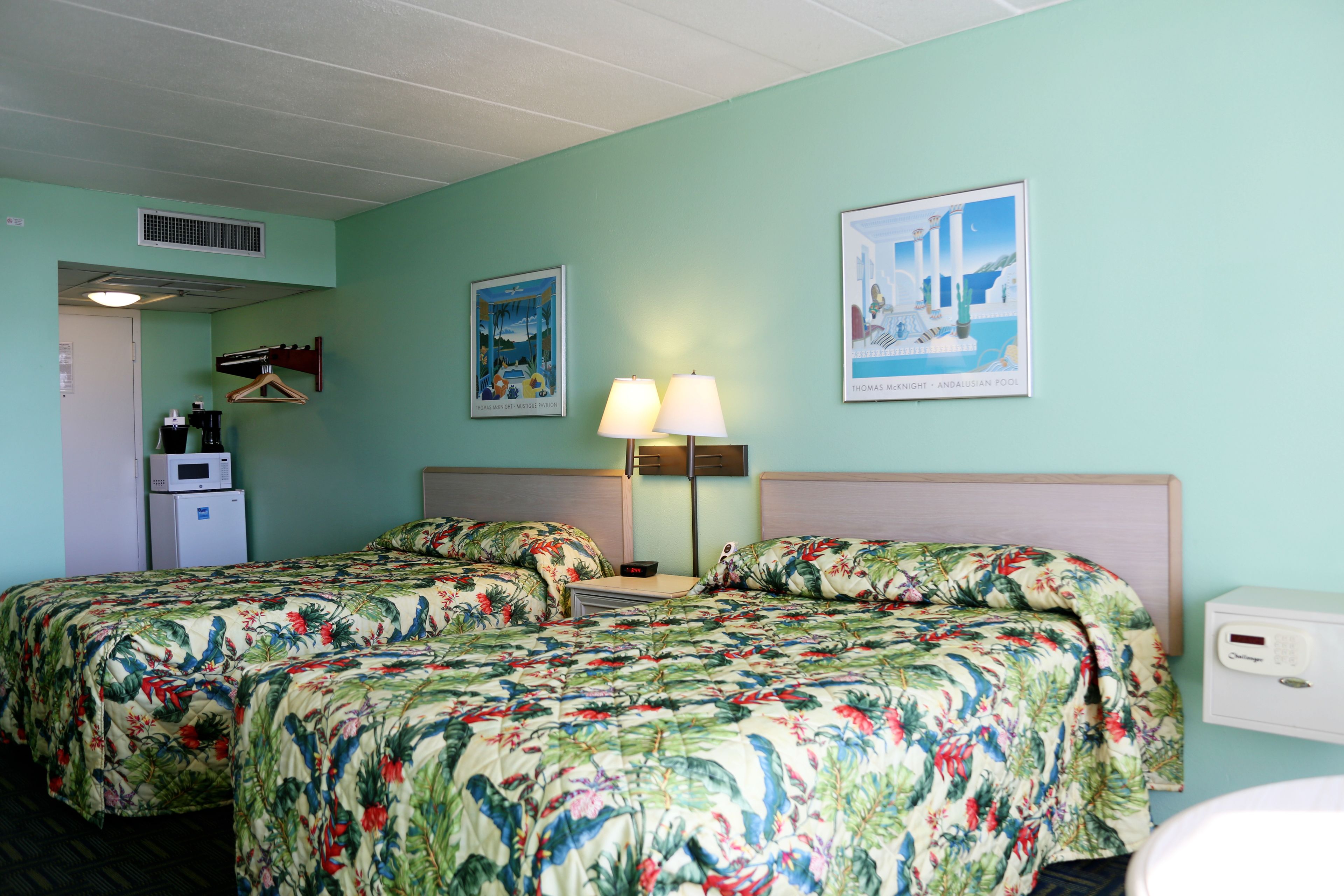 A hotel room with two beds, a desk, a lamp, and a picture of a pool.