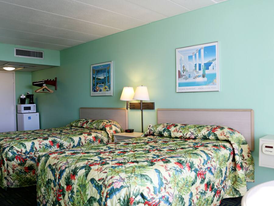 A hotel room with two beds, a desk, a lamp, and a picture of a pool.
