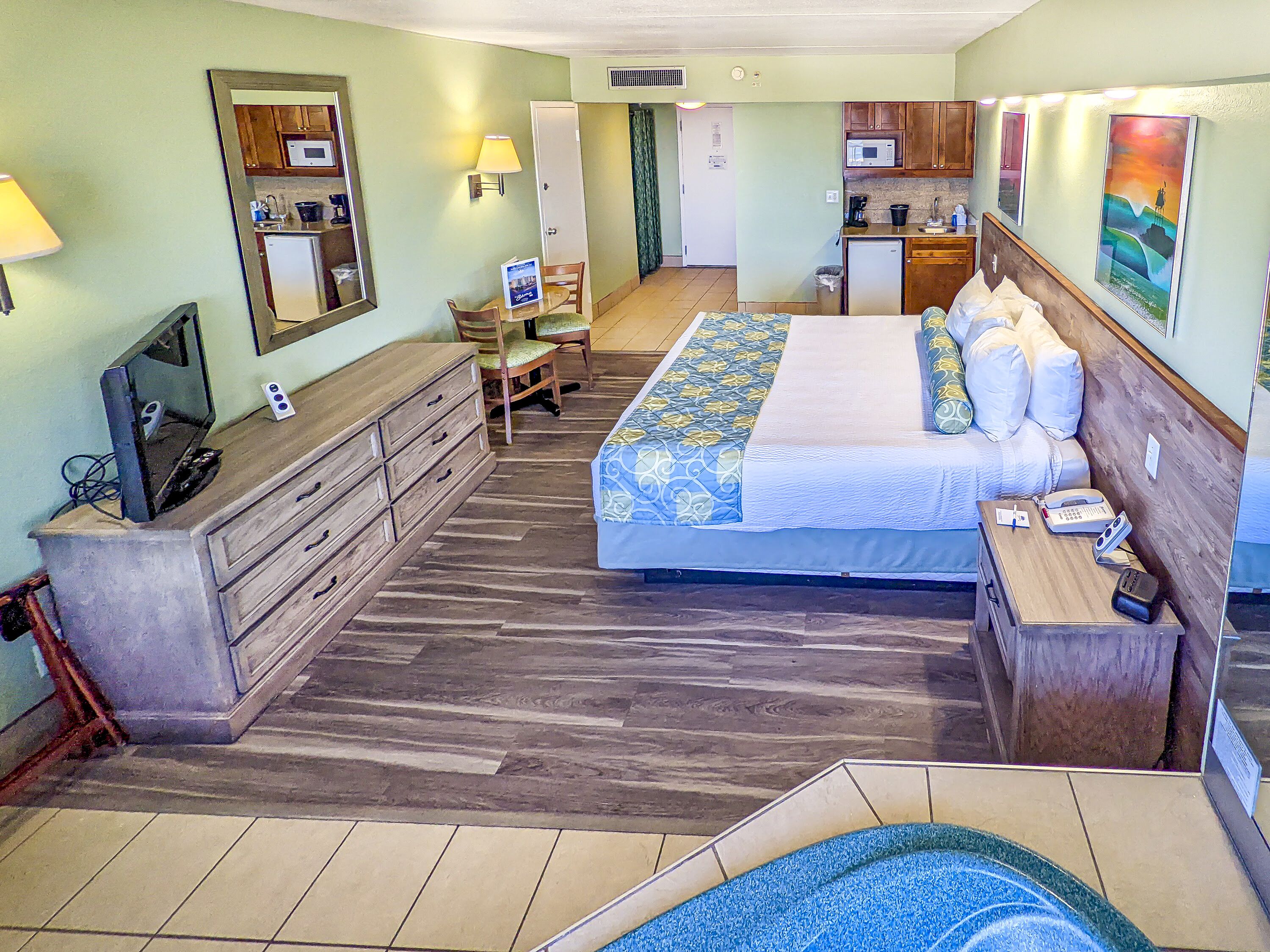 A hotel room with a bed, a desk, a dresser, a TV, a microwave, and a small kitchenette.