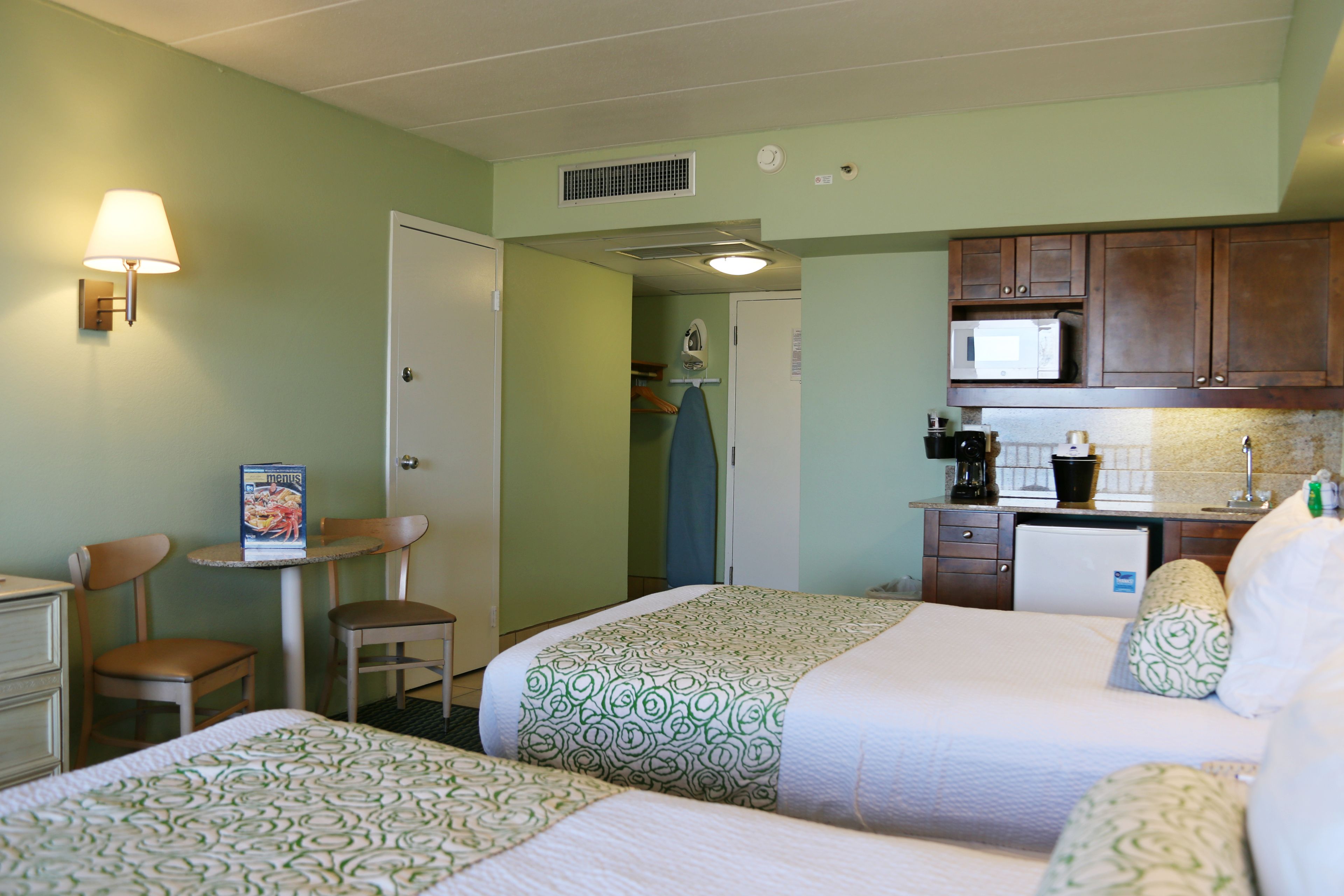 A hotel room with two beds, a desk, a chair, a microwave, and a kitchenette.