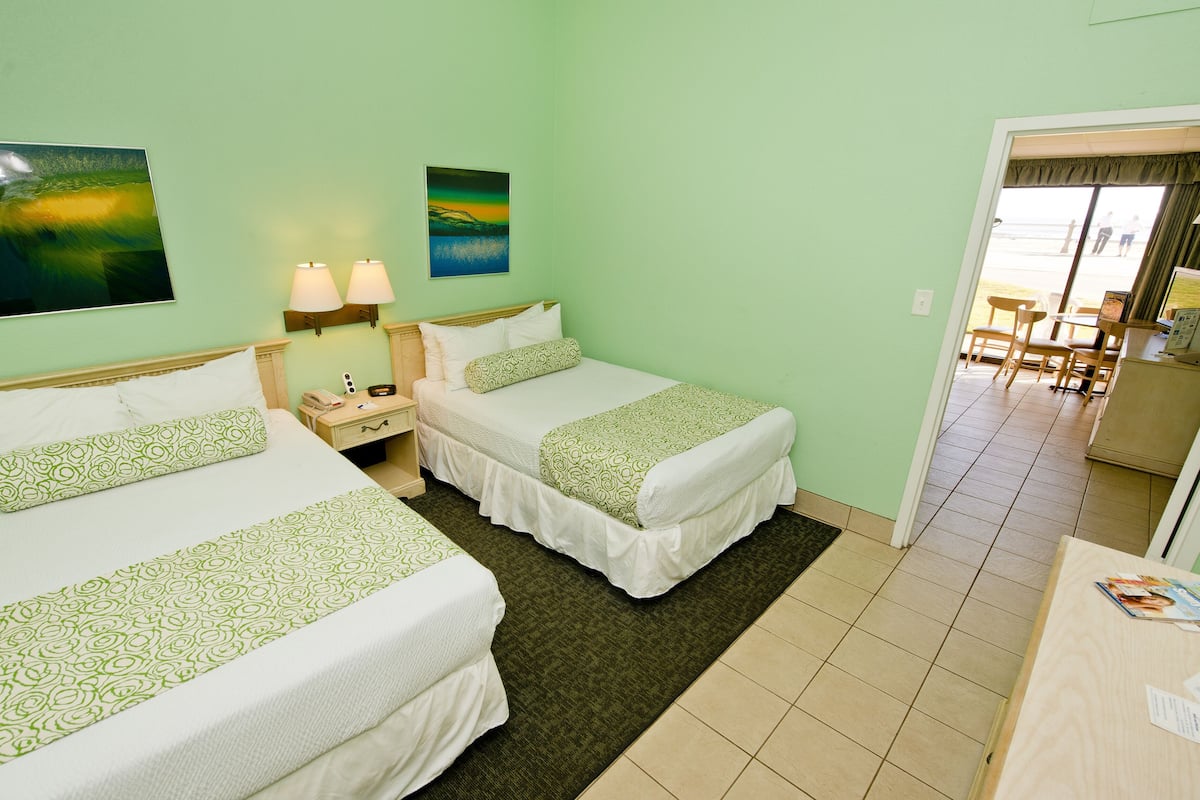 A hotel room with two beds, a small desk, and a view of the beach through the window.