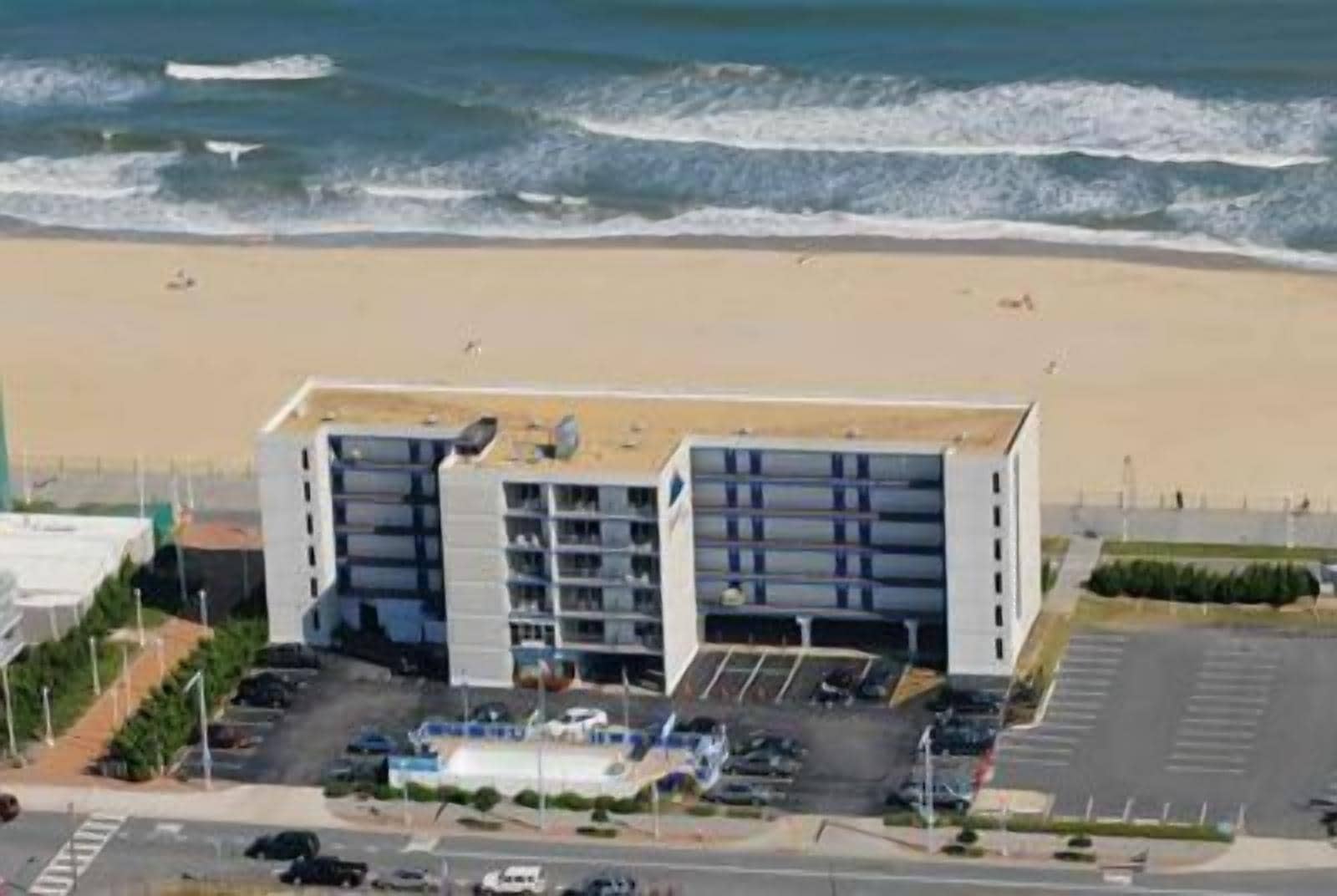 A coastal hotel with a modern design, featuring multiple floors and a parking area in front.