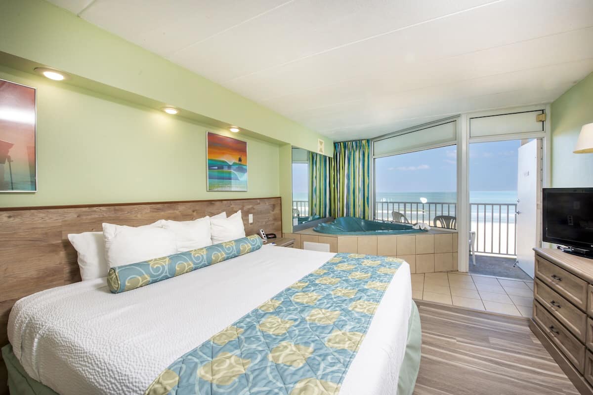 A hotel room with a large bed, a television, a balcony with a view of the sea, and a painting on the wall.