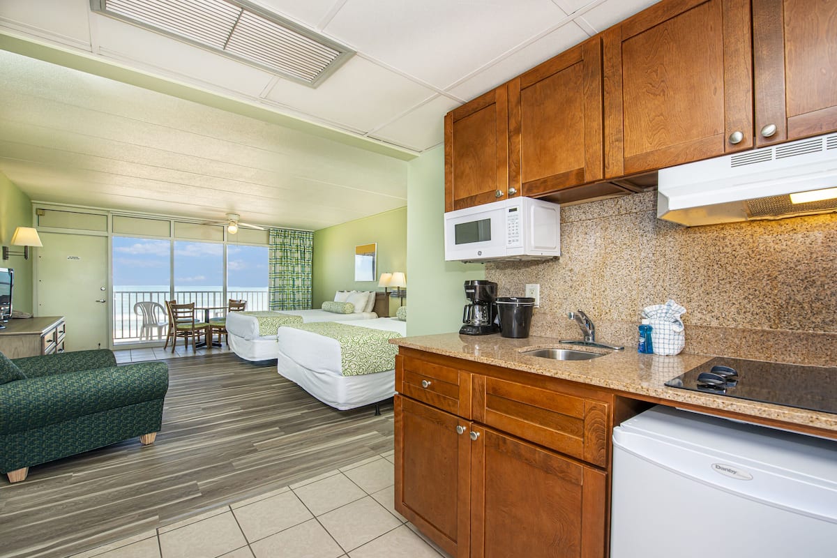 A hotel room with a kitchenette, a bed with a view, a green sofa, and a dining area with a view.