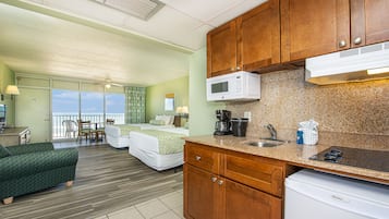 Habitación de hotel con kitchenette, cama con vista, sofá verde y zona de comedor con vista.