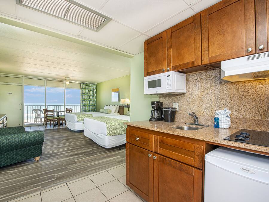 Habitación de hotel con kitchenette, cama con vista, sofá verde y zona de comedor con vista.