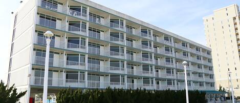 A multi-story hotel with balconies, a covered outdoor seating area, and a parking lot.