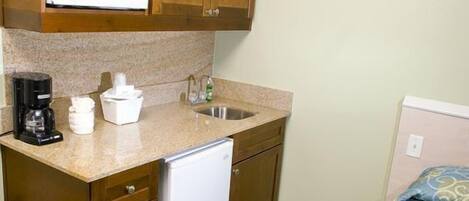 Una kitchenette compacta con microondas, cafetera y un refrigerador pequeño.