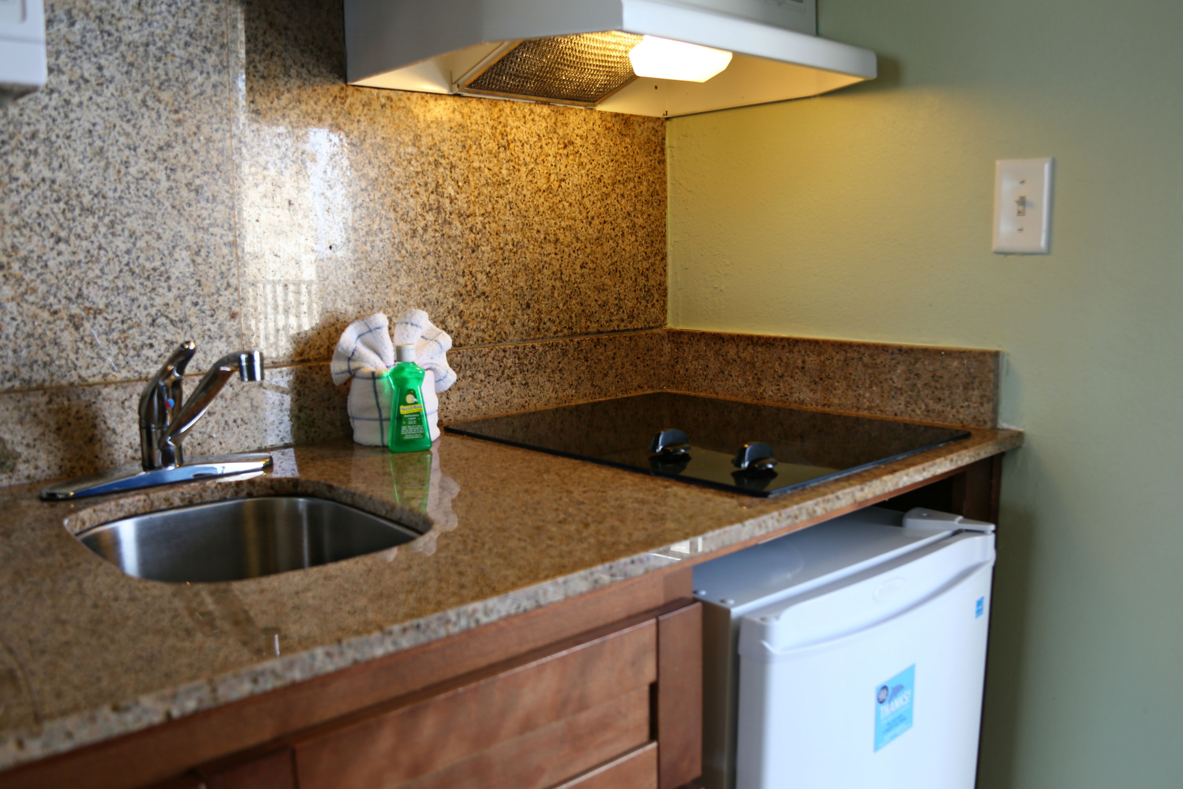 A kitchen with granite countertops, a stainless steel sink, and a white refrigerator.