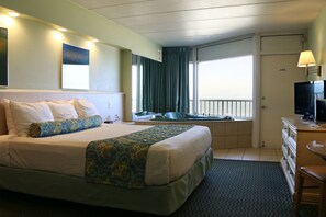 Una habitación de hotel con una cama grande, un escritorio con computadora, un televisor y una ventana con cortinas.