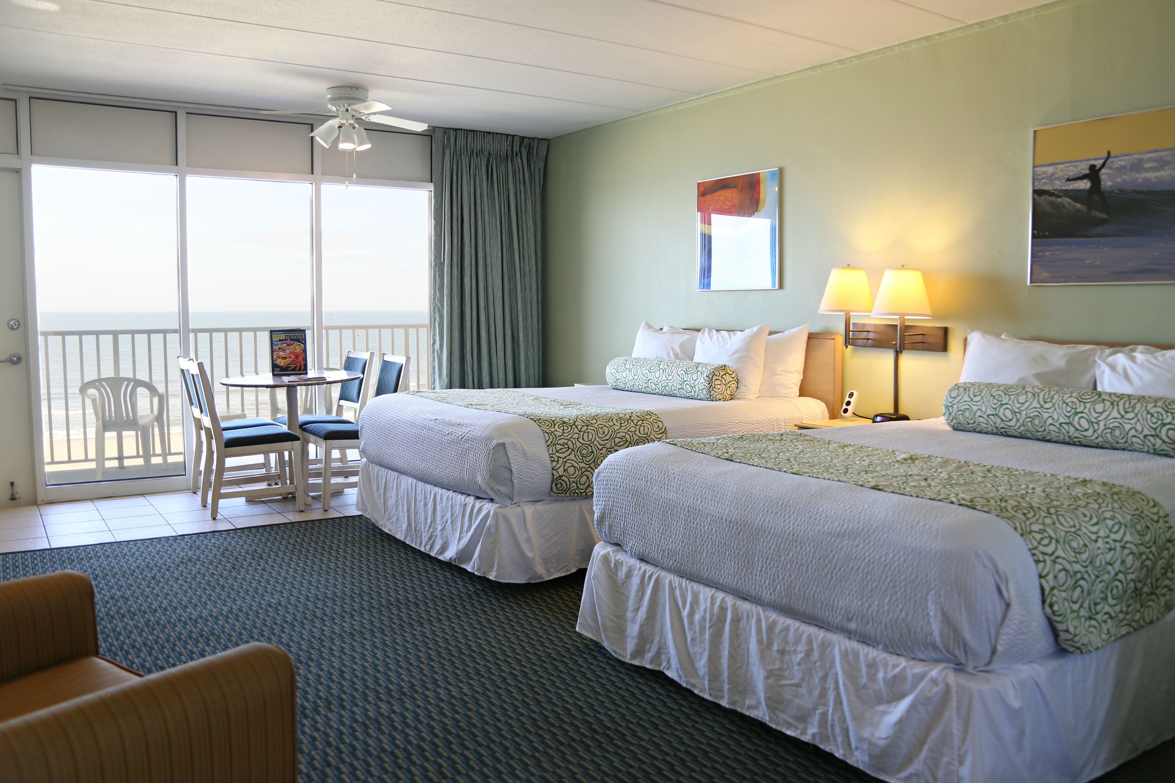 Quarto de hotel com duas camas, varanda com cadeiras e vista para o oceano.