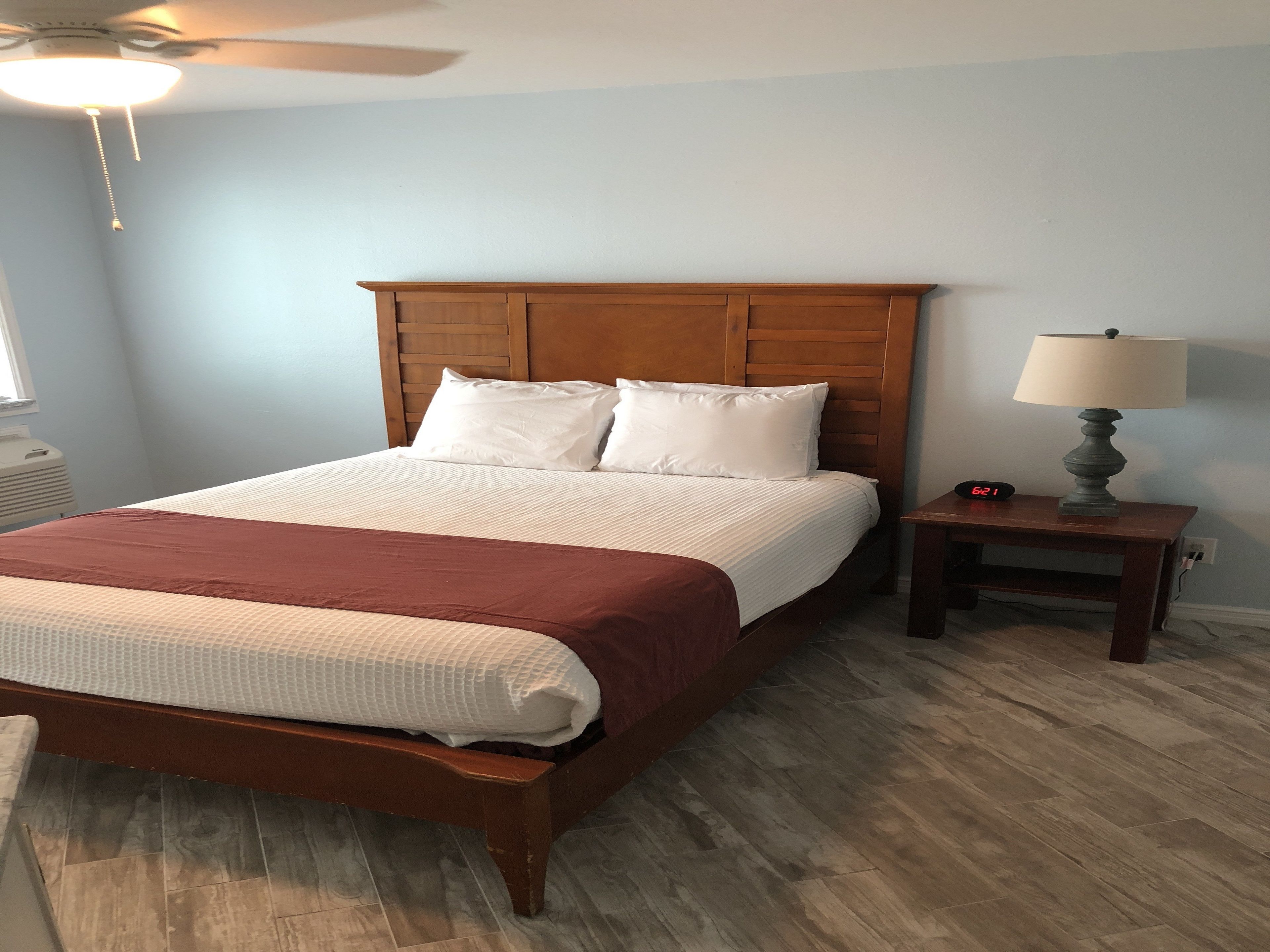 A neatly made bed with a wooden headboard, a bedside table with a lamp, and a clock.