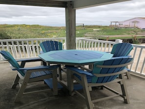 A covered outdoor seating area with a table and chairs, overlooking a grassy landscape and a building.