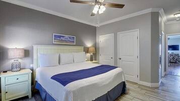 Une chambre à coucher avec un lit, des tables de chevet, un ventilateur de plafond et une porte.