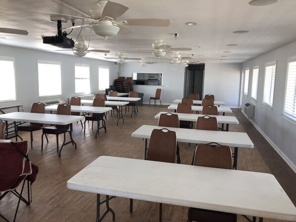 A classroom with white tables and brown chairs, ceiling fans, and large windows.
