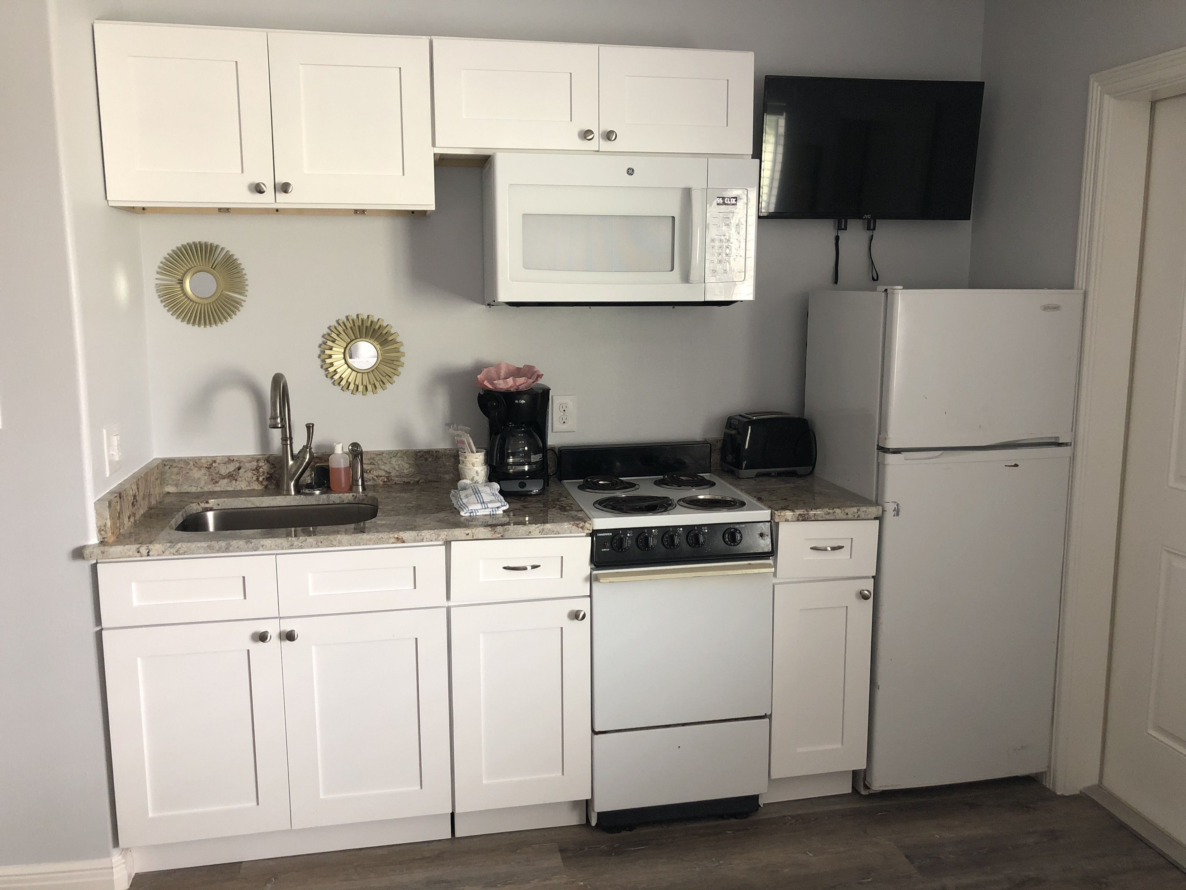 A kitchen with white cabinets, a microwave, a stove, a toaster, and a refrigerator.