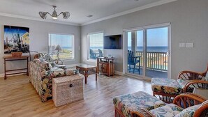 A spacious living room with a large sliding glass door leading to a balcony, a sofa set, and a small table. - Beachgate CondoSuites and Oceanfront Resort (Port Aransas)