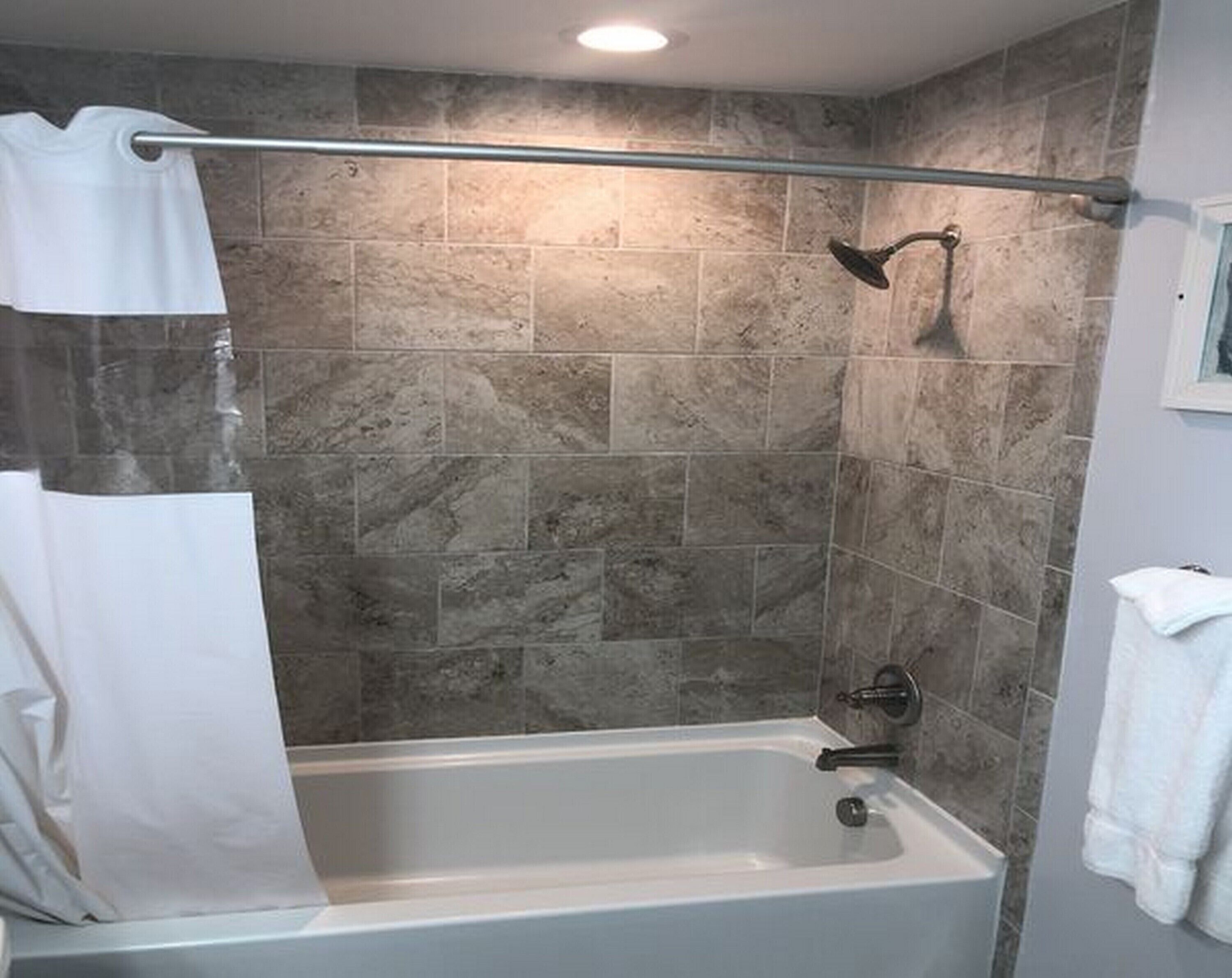 A bathroom with a bathtub, shower, and tiled walls.