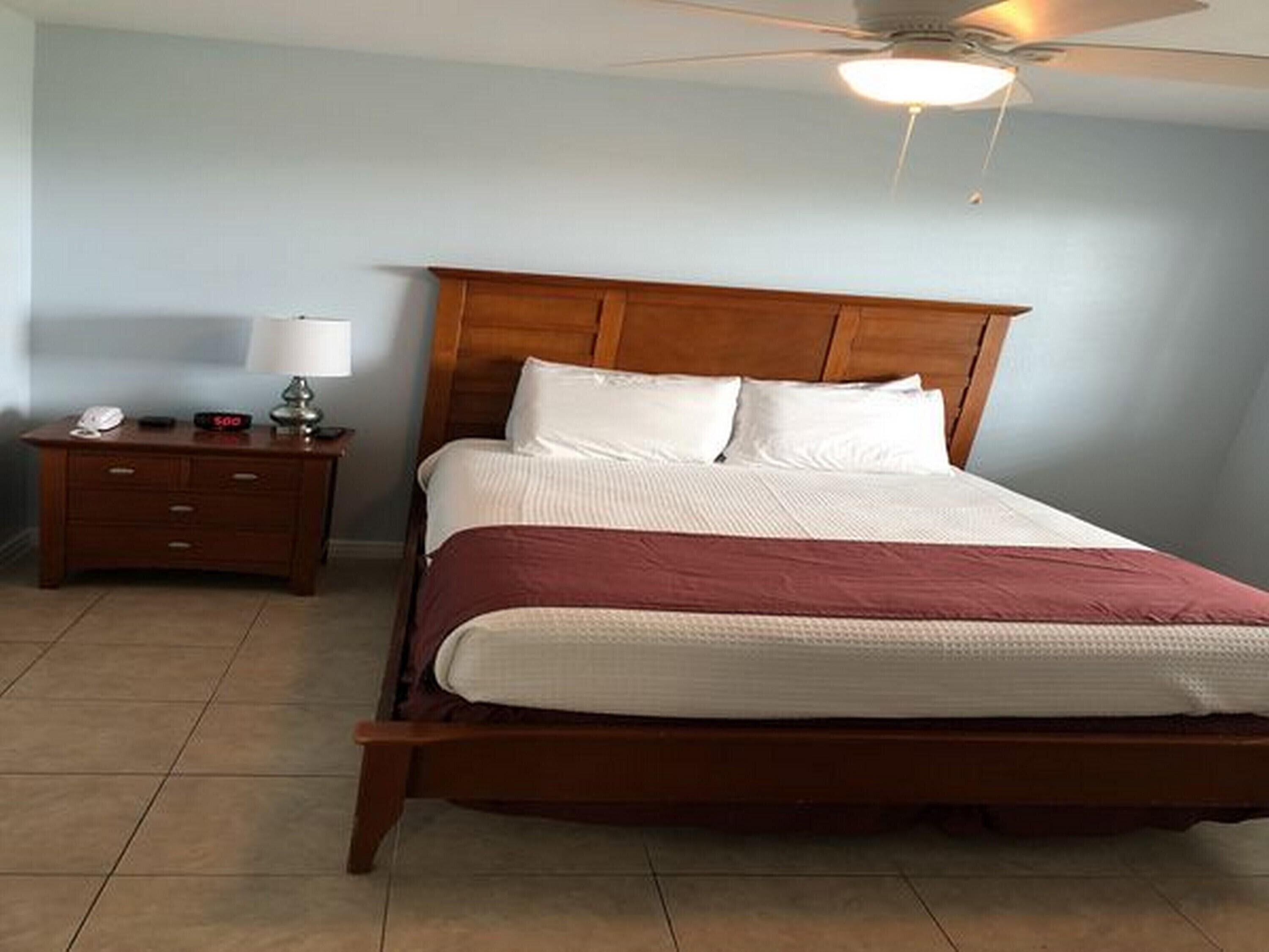 Un dormitorio con una cama de madera, una mesita de noche con lámpara y un ventilador de techo.
