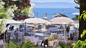 Un espace extérieur aménagé pour les repas, avec des tables et des chaises, donnant sur un plan d’eau.