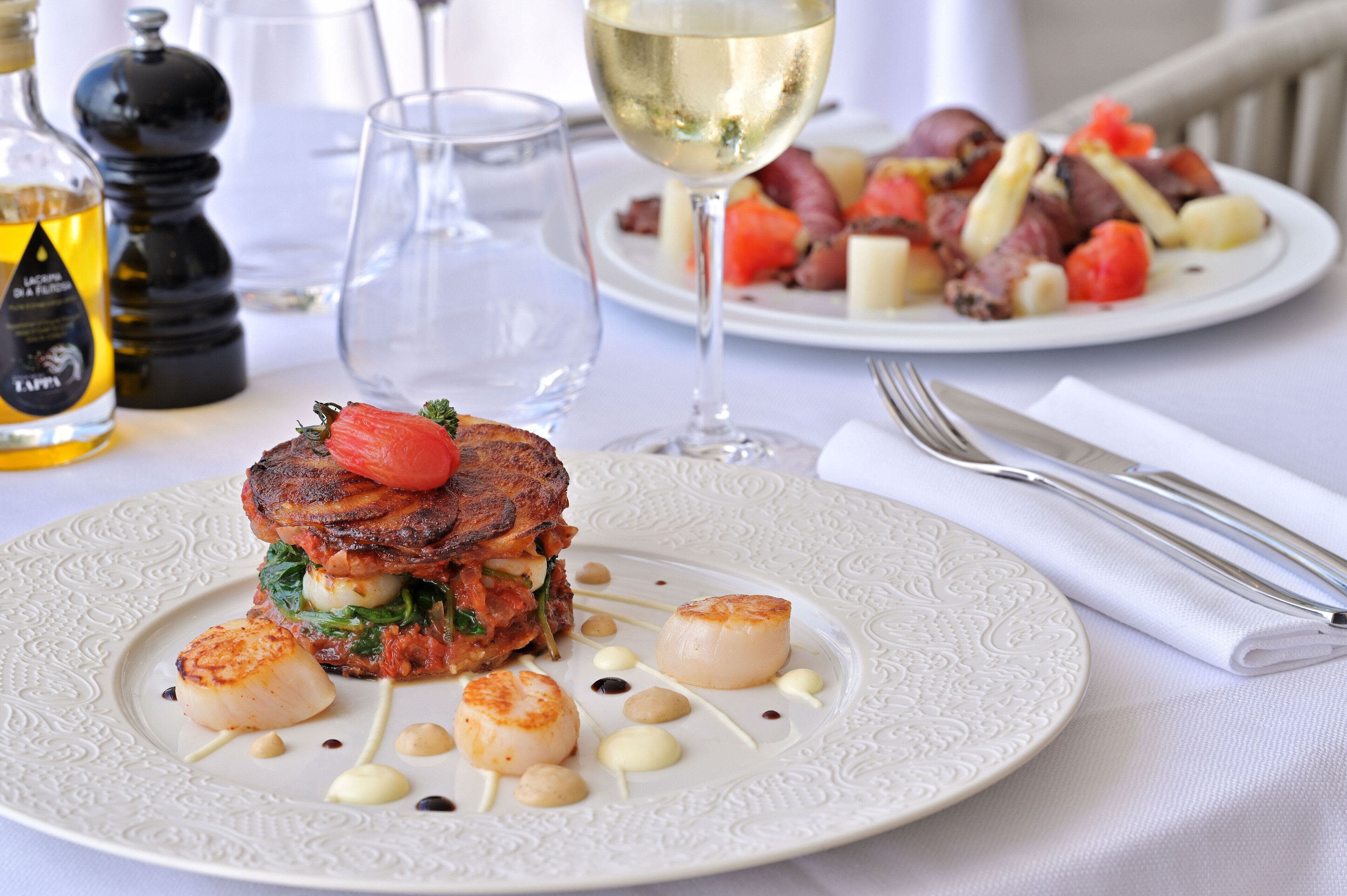 A dining table with plates of food, a wine glass, and cutlery.