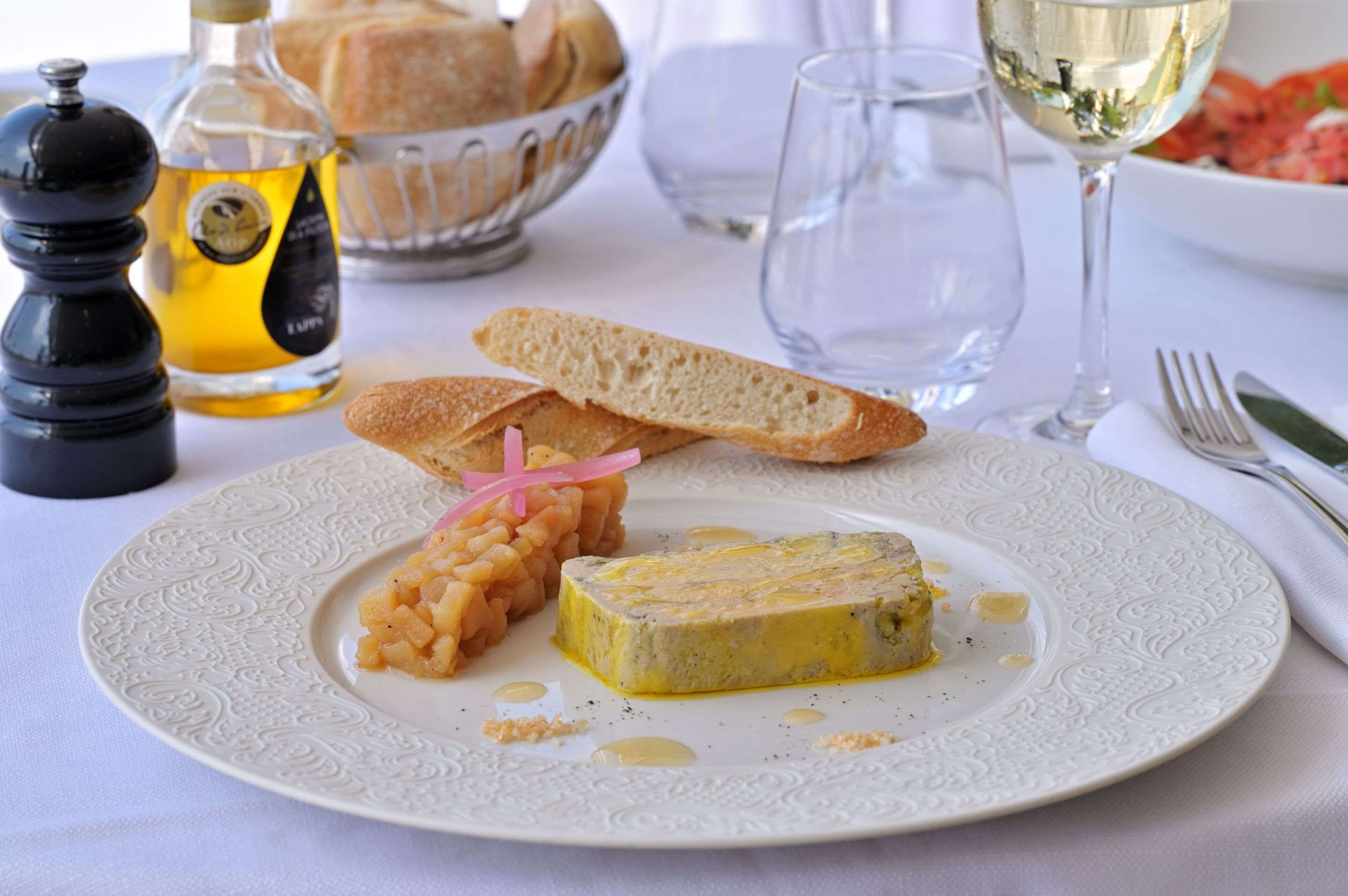 A plate with a slice of cheese, bread, and a small dish of pickles.