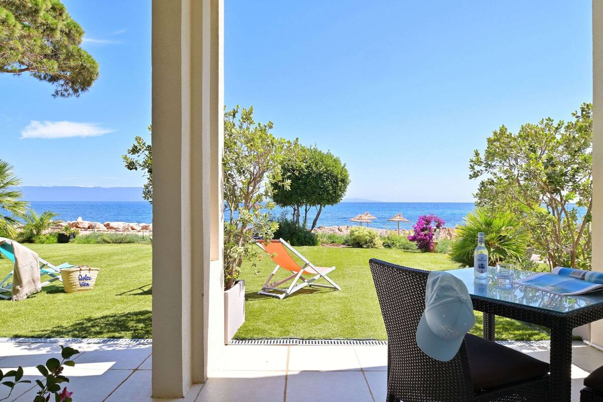 Eine Terrasse mit einem Glastisch, einem Korbstuhl und Blick aufs Meer.