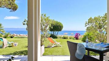 Une terrasse avec une table en verre, un fauteuil en osier et une vue sur la mer.
