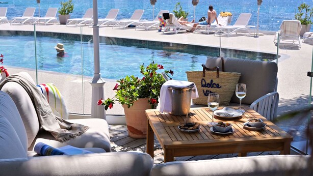 Un espace aménagé au bord de la piscine, avec des chaises longues, une table où sont servis des plats et des boissons, et une vue sur la mer.