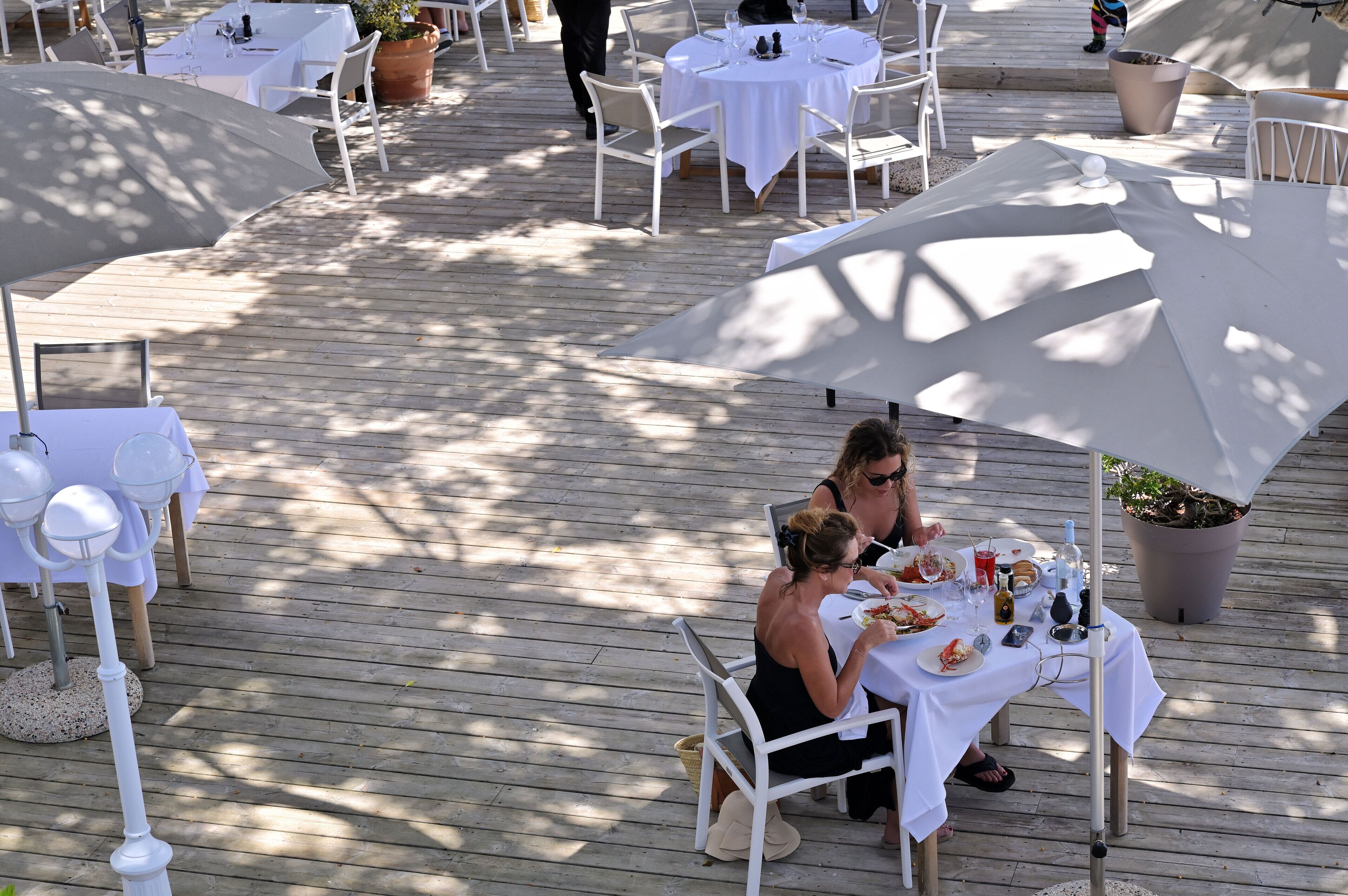Een terras met tafels, stoelen, parasols en potplanten.