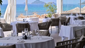 Un restaurant en bord de mer, avec des tables rondes disposées pour accueillir les clients, offrant une vue sur l’océan.