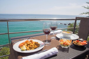 Una mesa de comedor con platos de comida, copas de vino y vista al océano.