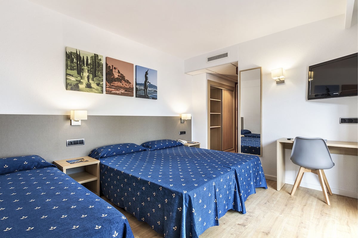 A hotel room with two beds, a desk, a chair, and a TV.