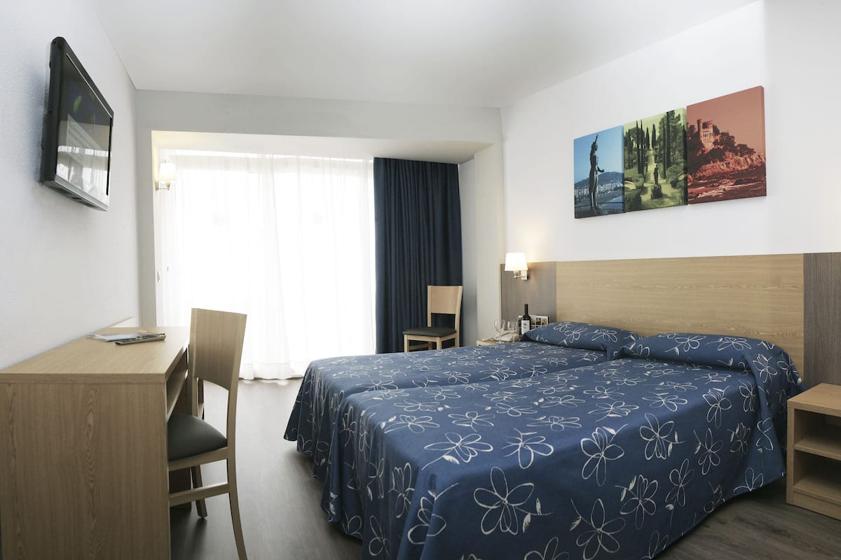 A hotel room with a bed, a desk, a chair, and a painting on the wall.
