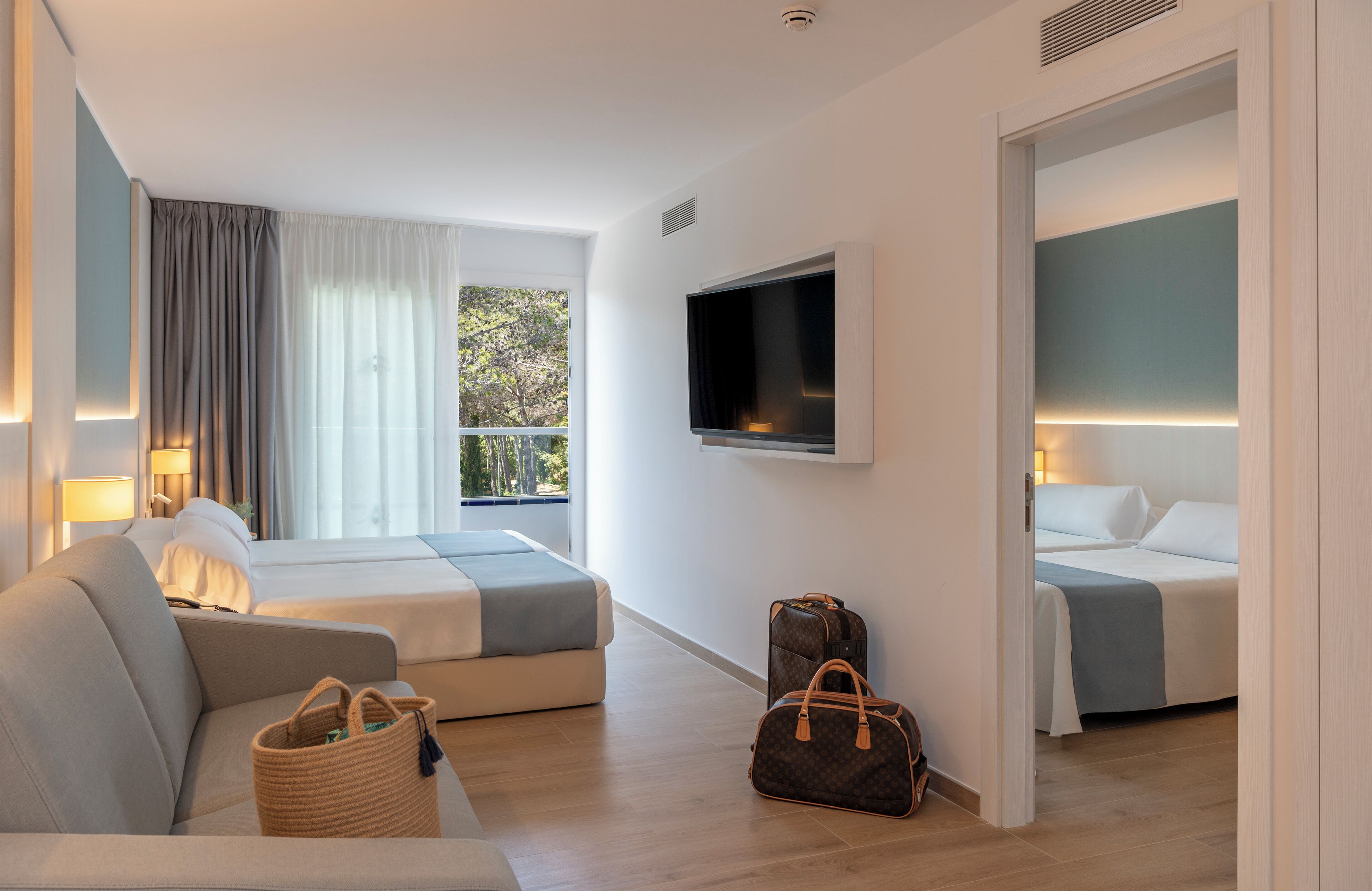 Een moderne hotelkamer met twee bedden, een bank, een televisie en een raam met gordijnen.