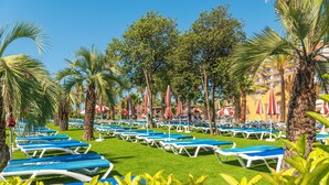 A poolside area with rows of sun loungers and palm trees. - Costa Encantada Suites & Resort (Lloret de Mar)