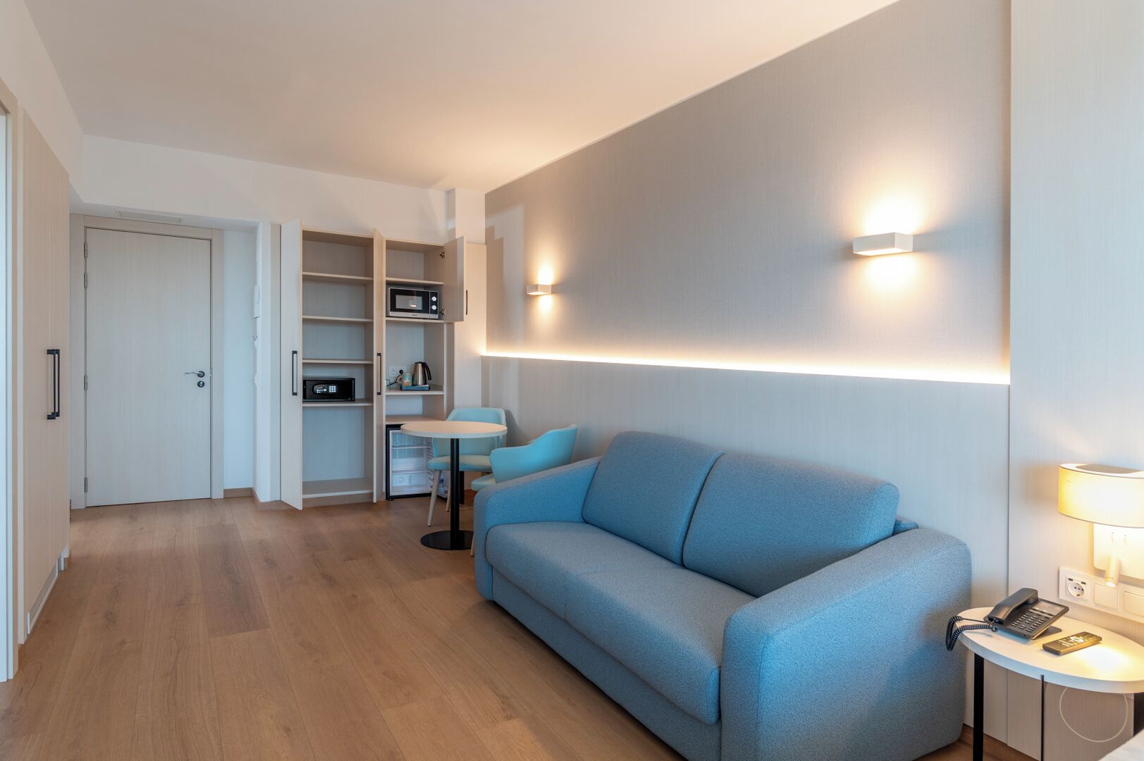 Une chambre d’hôtel moderne équipée d’un canapé, d’une petite table, d’un four à micro-ondes et d’une armoire.