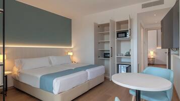 Una habitación de hotel con cama, escritorio, silla, microondas y televisor.