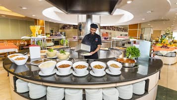 Montaje de bufé con diferentes alimentos y un cocinero sirviendo.