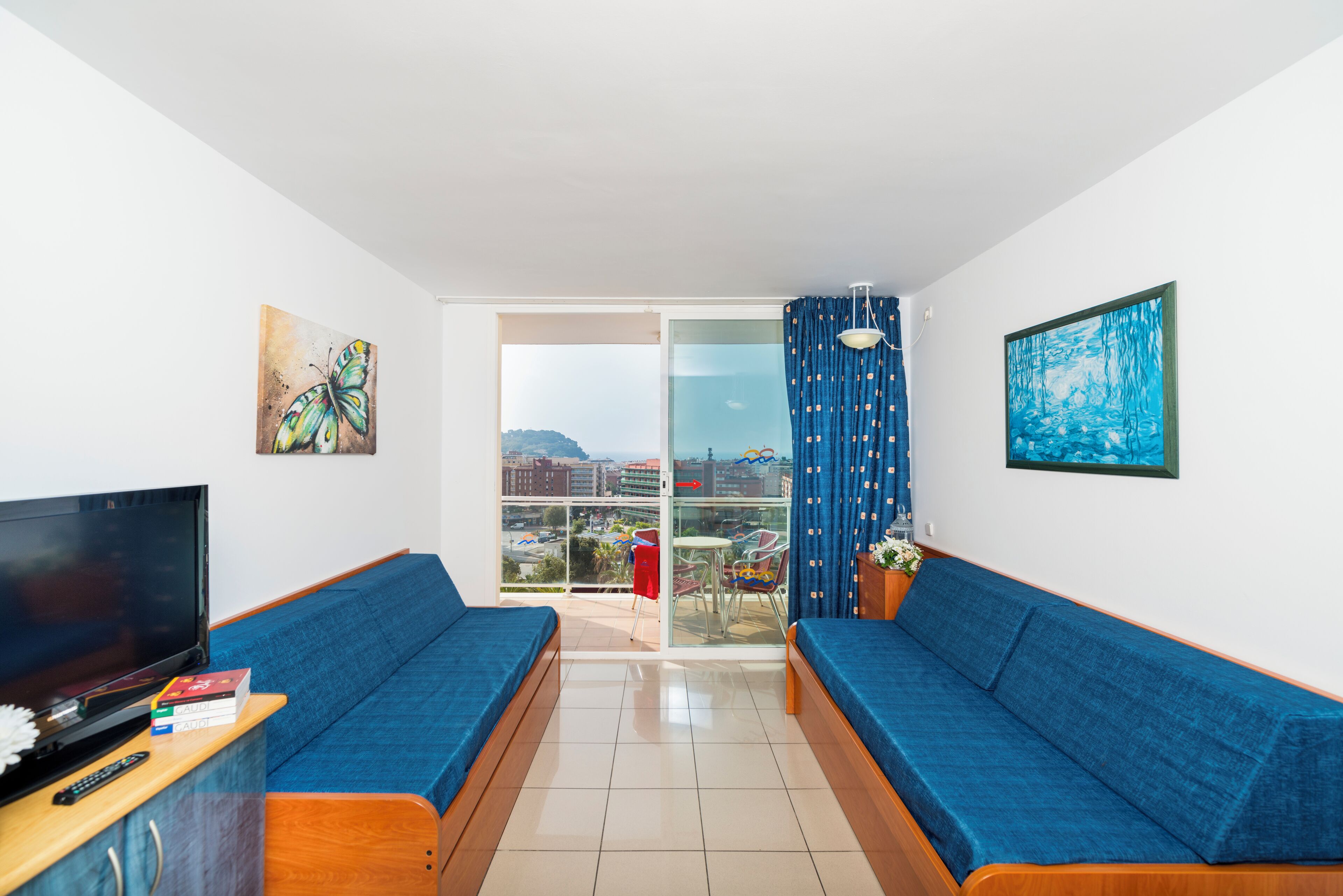 Un salon moderne avec deux canapés bleus, un téléviseur et des œuvres d’art accrochées aux murs.