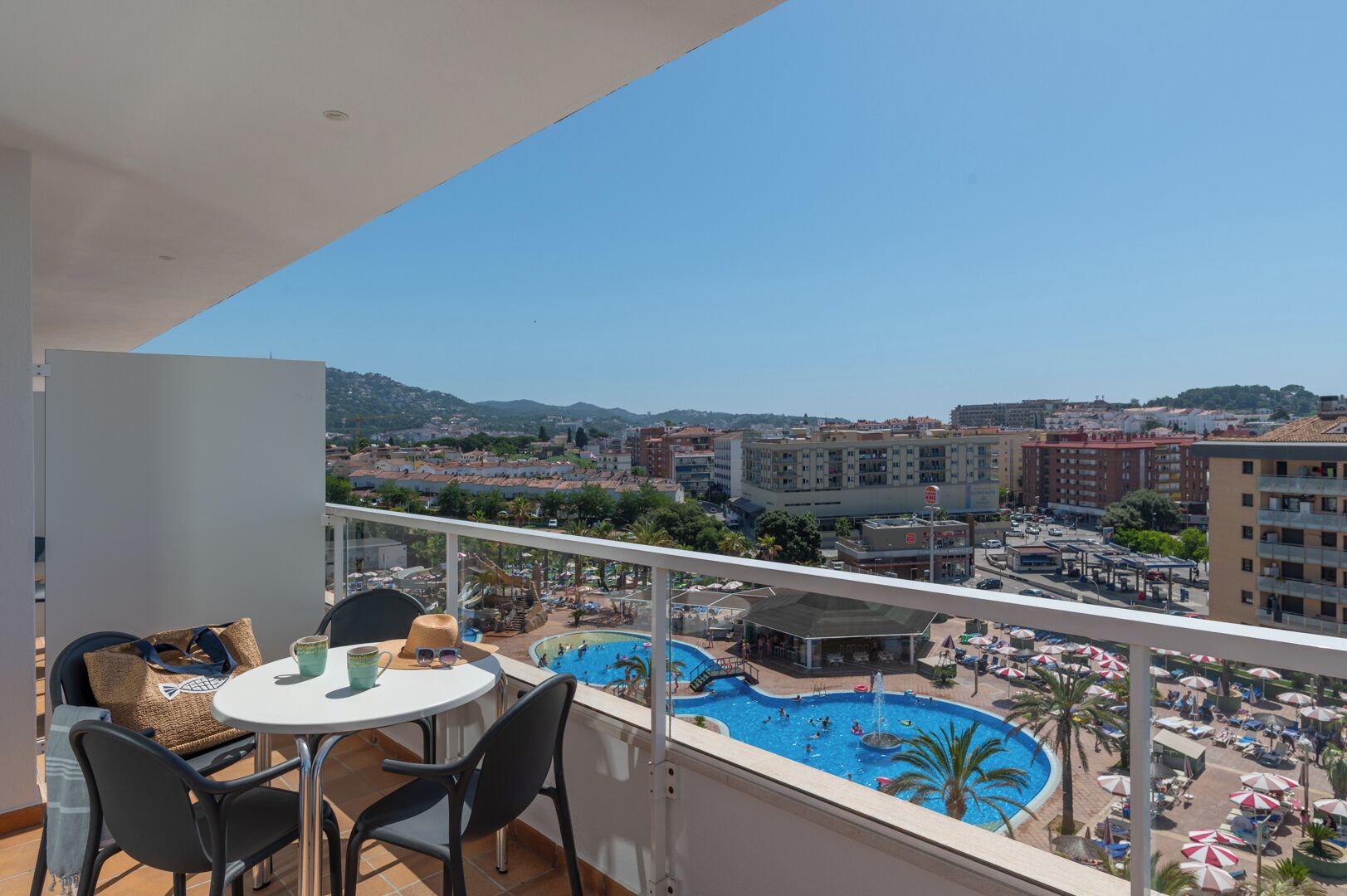 Ein Balkon mit Tisch und Stühlen mit Blick auf einen Pool und eine Stadtansicht.