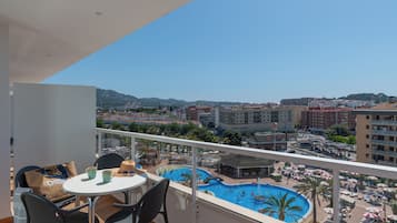 Ein Balkon mit Tisch und Stühlen mit Blick auf einen Pool und eine Stadtansicht.